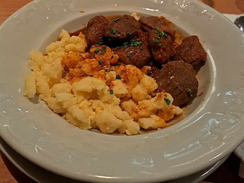 Chicken gizzards braised in a red paprika sauce, served with buttered spaetzle and chives in a white bowl