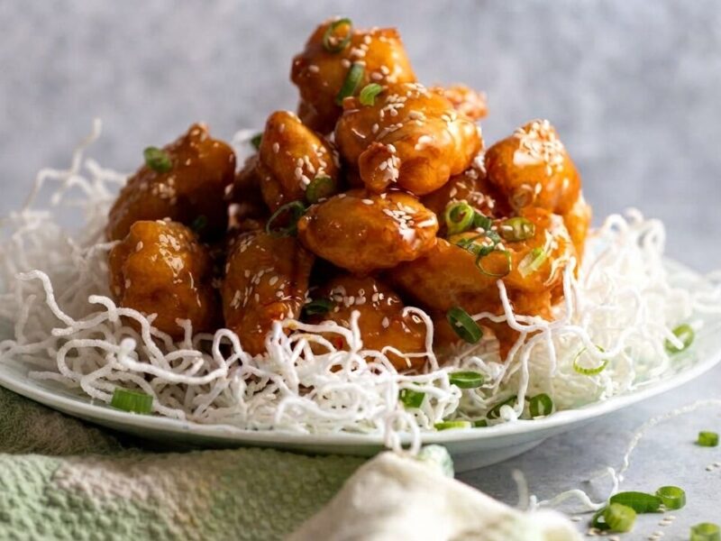 chinese honey garlic chicken glossy sticky glazed pieces served on a white plate with sesame seeds and scallions