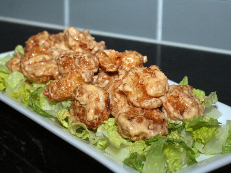 Homemade bang bang shrimp coated in creamy sweet chili sauce on a white platter of chopped romaine