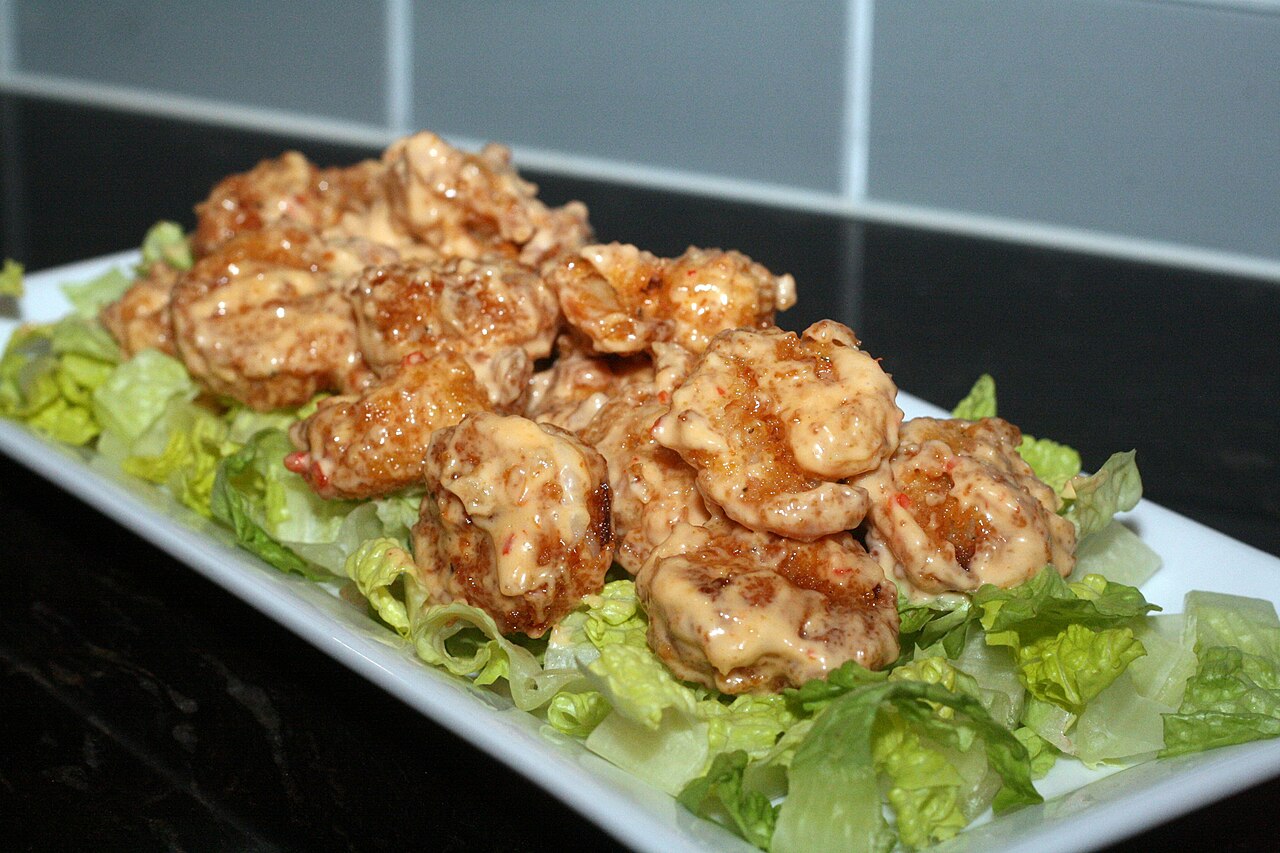 Homemade bang bang shrimp coated in creamy sweet chili sauce on a white platter of chopped romaine