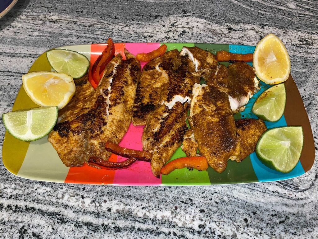 Blackened tilapia fillets coated in Cajun spices on a platter with lime and lemon wedges