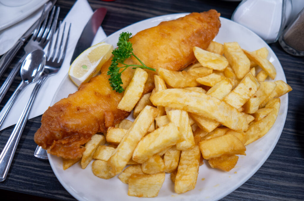 Battered fish fillet with thick-cut chips, lemon wedge and parsley on a white plate