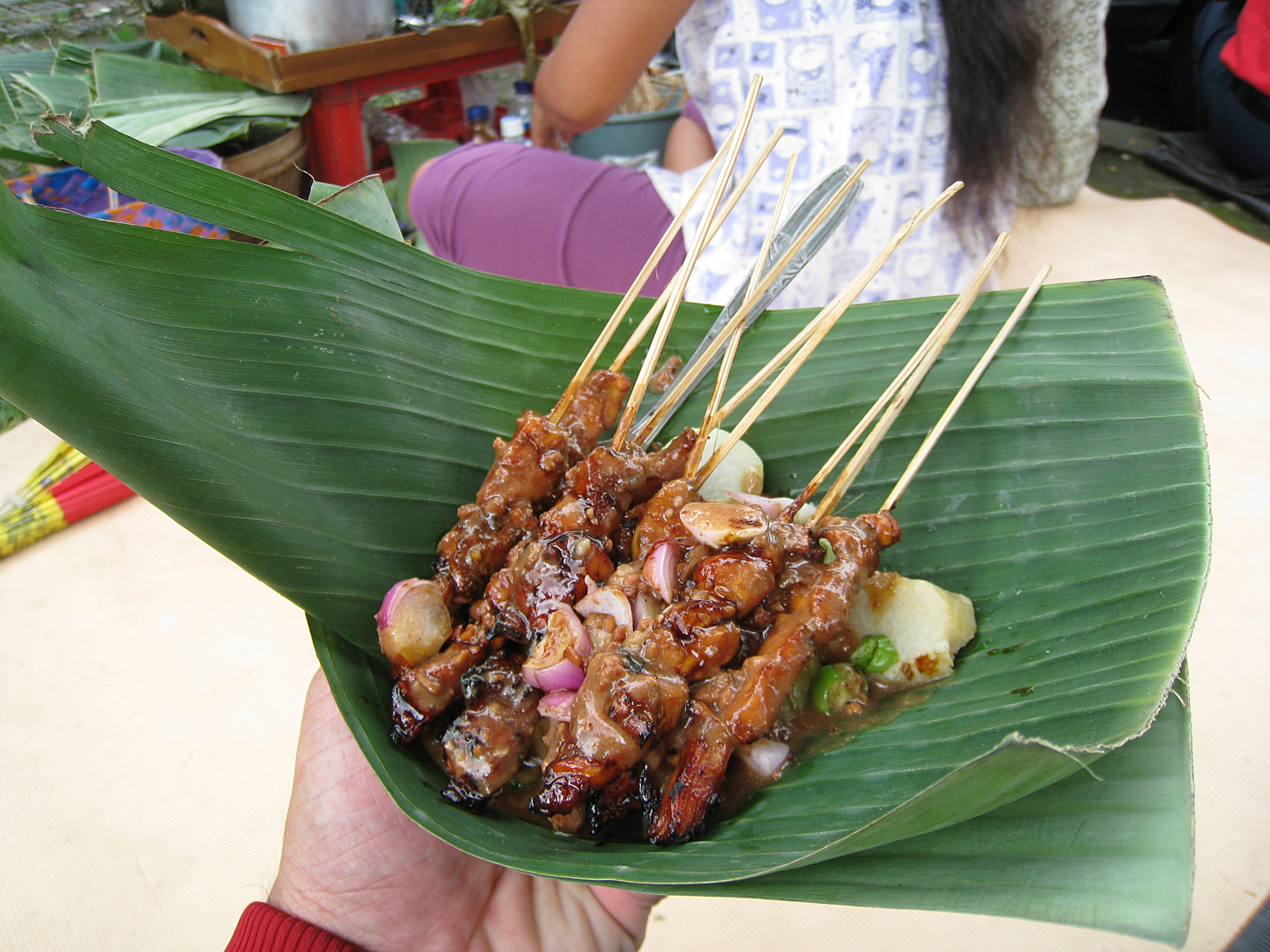 Glazed chicken satay skewers piled on a banana leaf