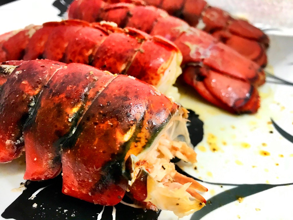 Four cooked lobster tails with red shells charred dark in spots