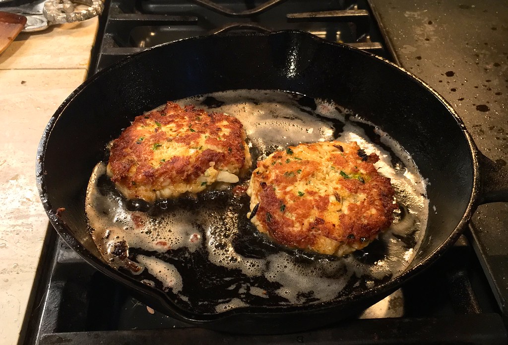 Two crab cakes browning in shallow butter and oil in a cast-iron skillet