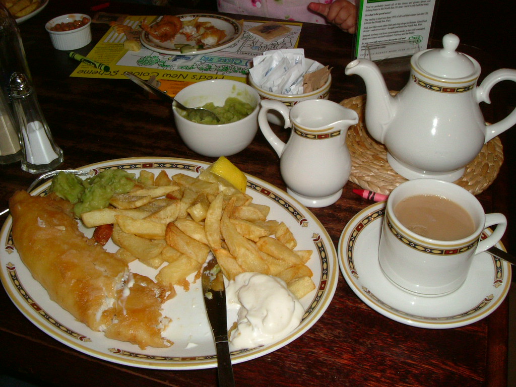 Plate of battered fish and chips with mushy peas, tartare sauce and a pot of tea
