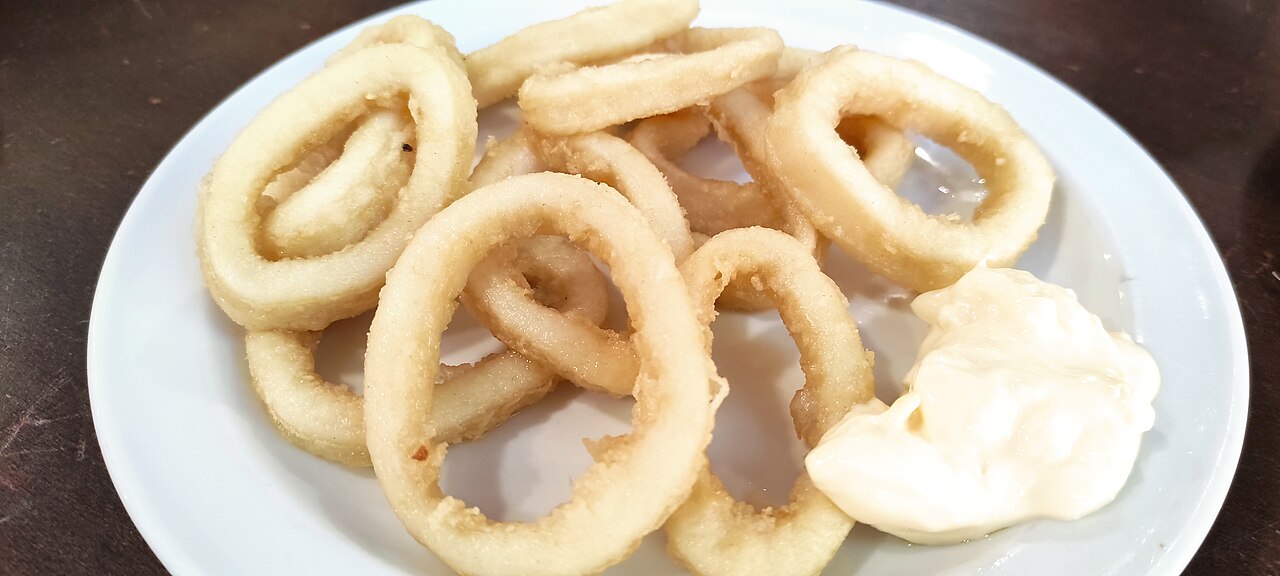 Plate of golden fried calamari rings with a spoonful of mayonnaise on the side