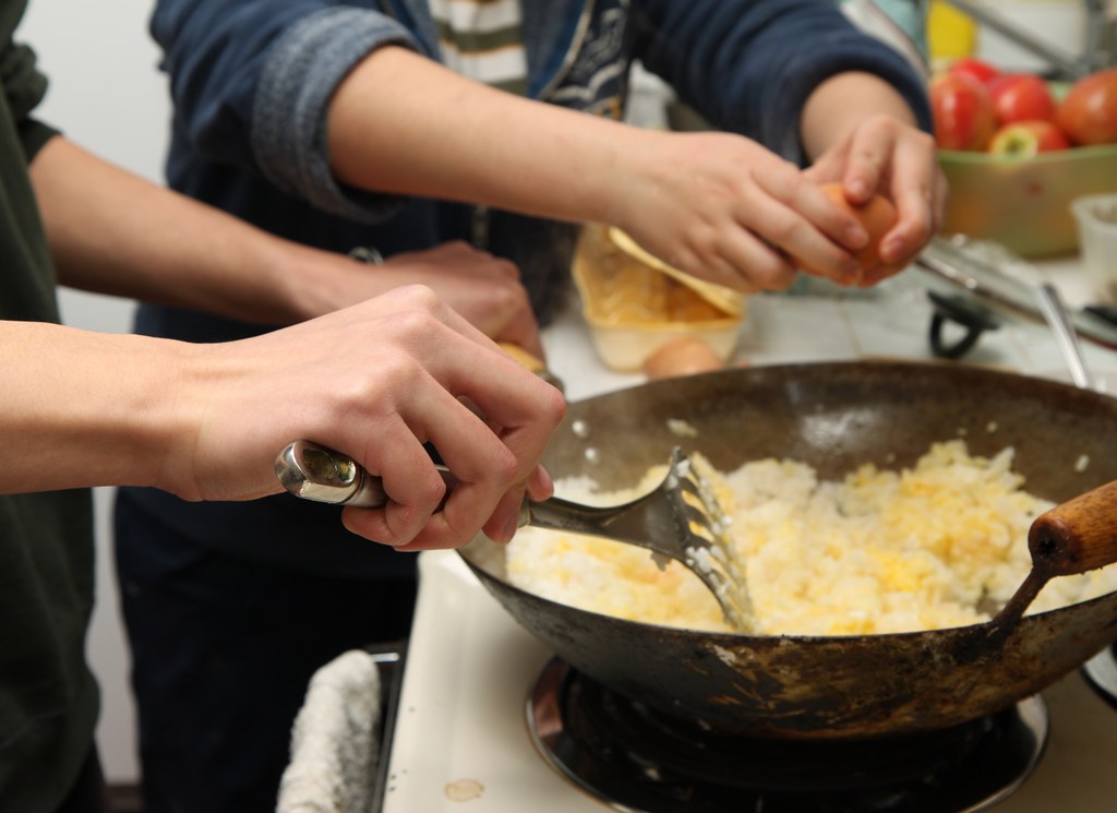 Rice and scrambled egg being tossed with a spatula in a carbon-steel wok on a home gas burner