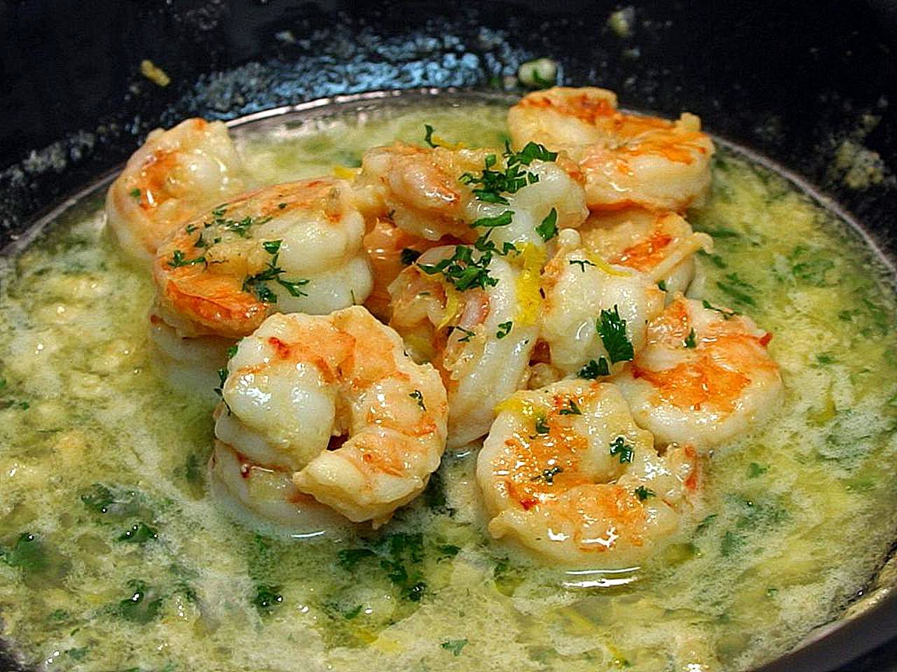 Shrimp scampi in a skillet of foaming garlic butter with chopped parsley and lemon zest