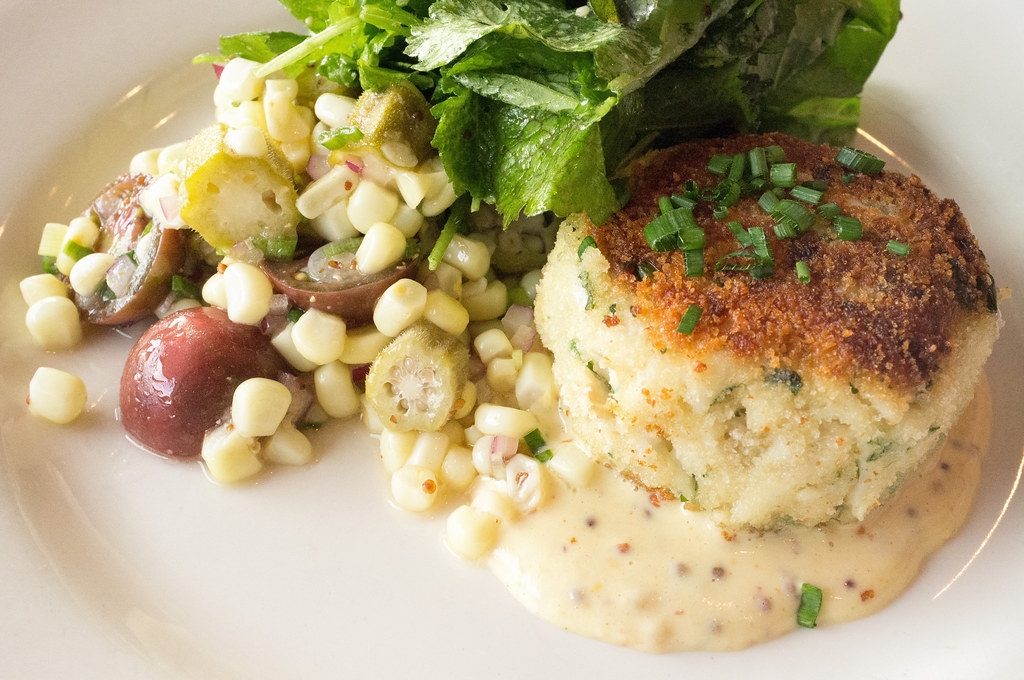 Golden jumbo lump crab cake with visible chunks of crab, served with corn salad and mustard sauce