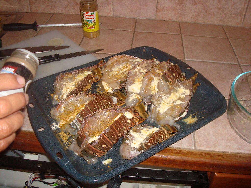 Raw lobster tails split open and spread with butter on a baking tray before cooking