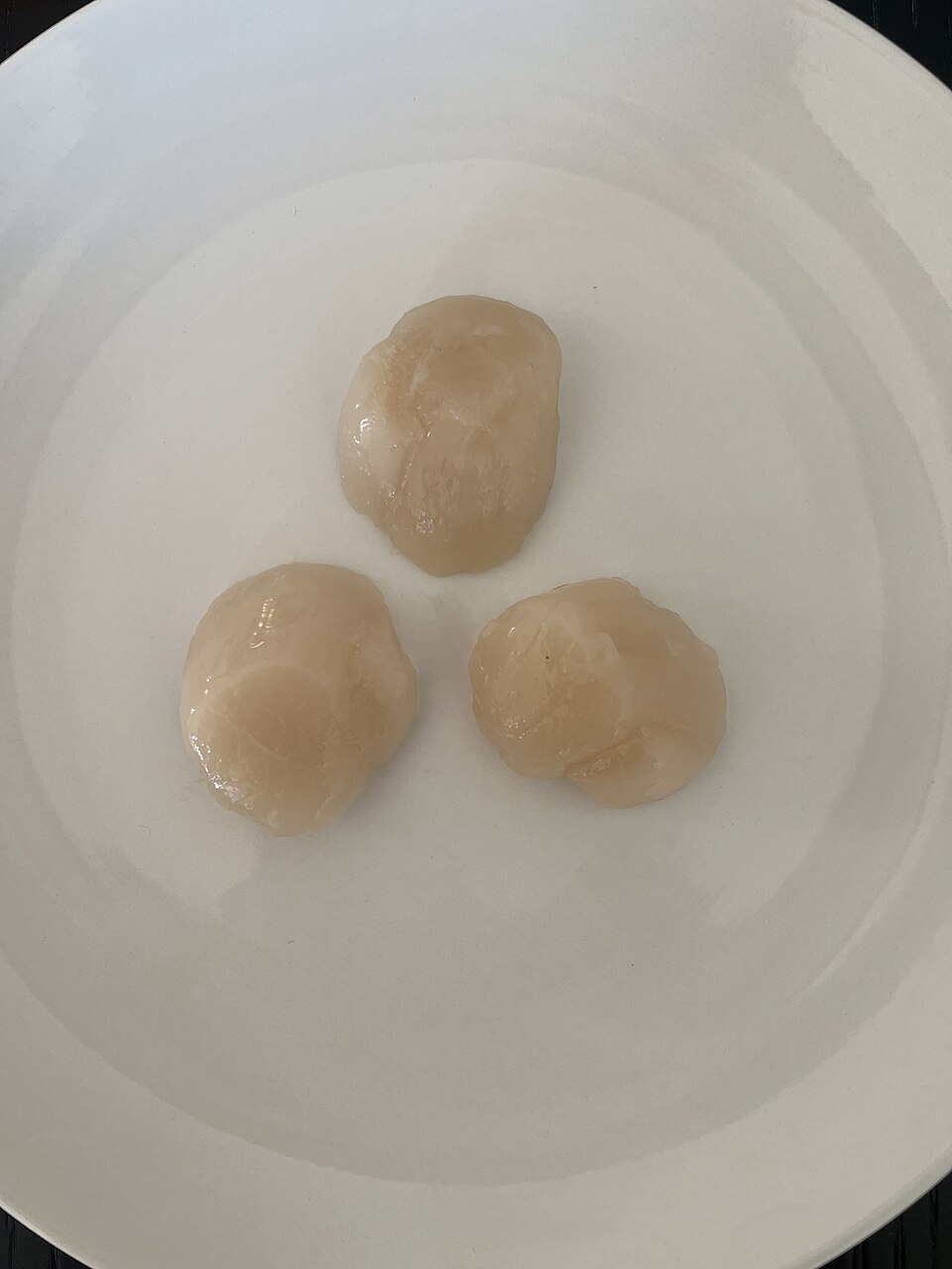 Three raw fresh sea scallops on a white plate