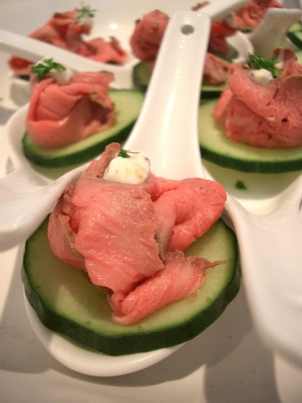 Rare roast beef canapes on cucumber rounds served on white tasting spoons
