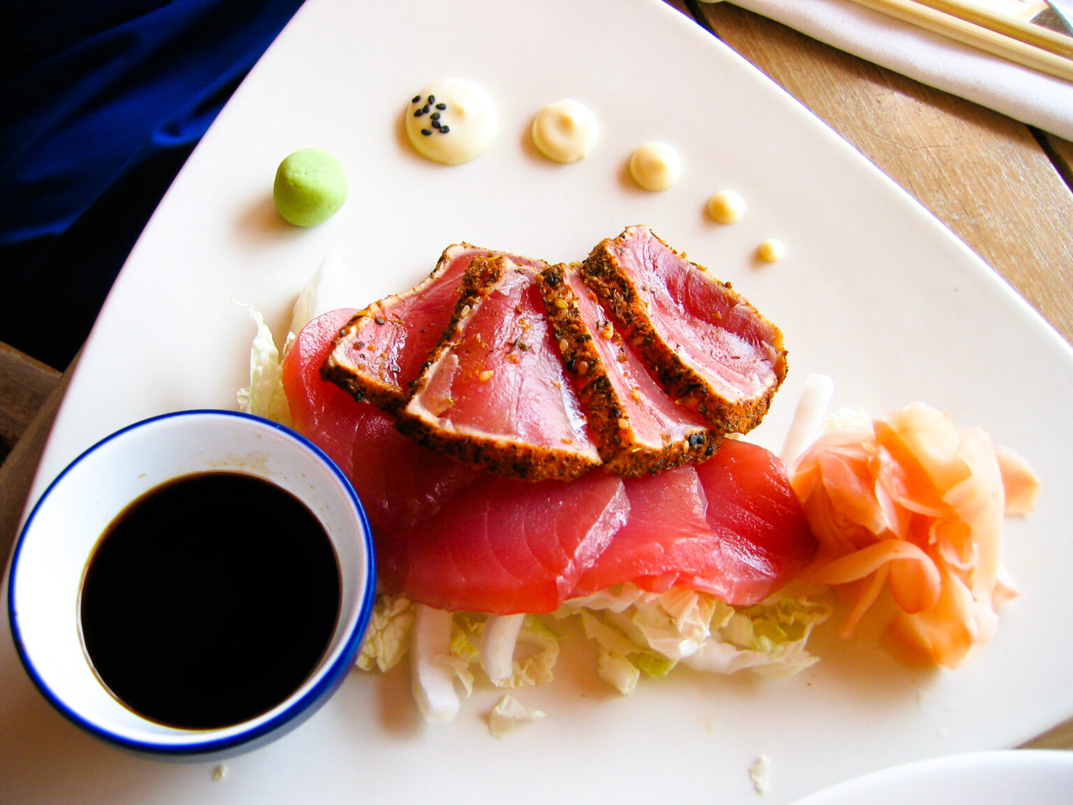 Seared ahi tuna slices with a peppered crust laid over raw tuna slices, with soy sauce, wasabi and pickled ginger