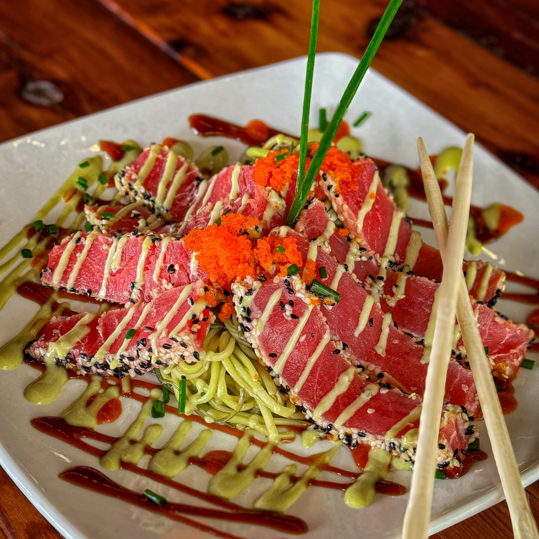 Sliced sesame-crusted seared ahi tuna with rare red centers fanned over soba noodles, topped with masago and chives