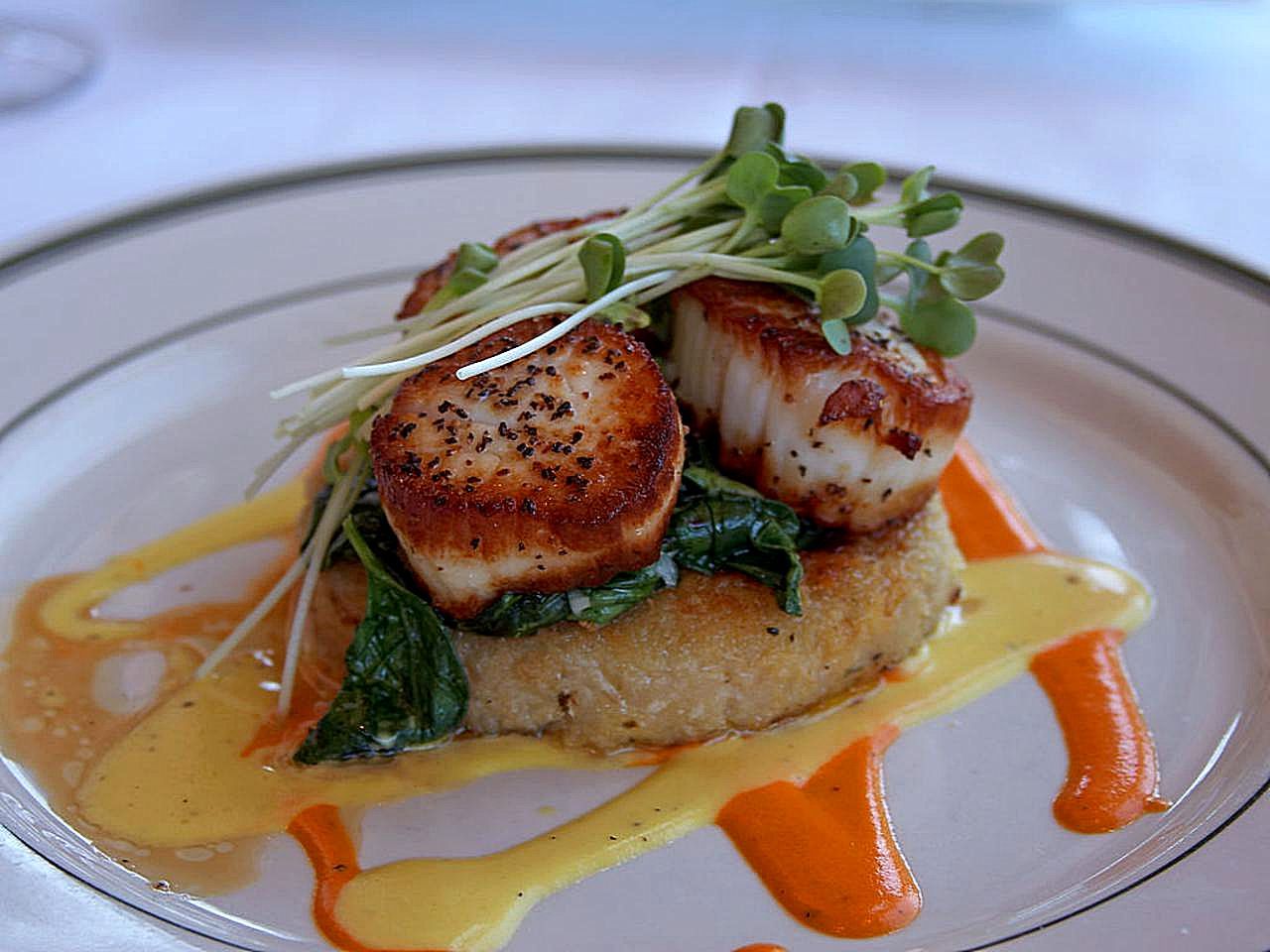 Two seared scallops with a browned crust and cracked black pepper on a bed of greens with microgreens on top