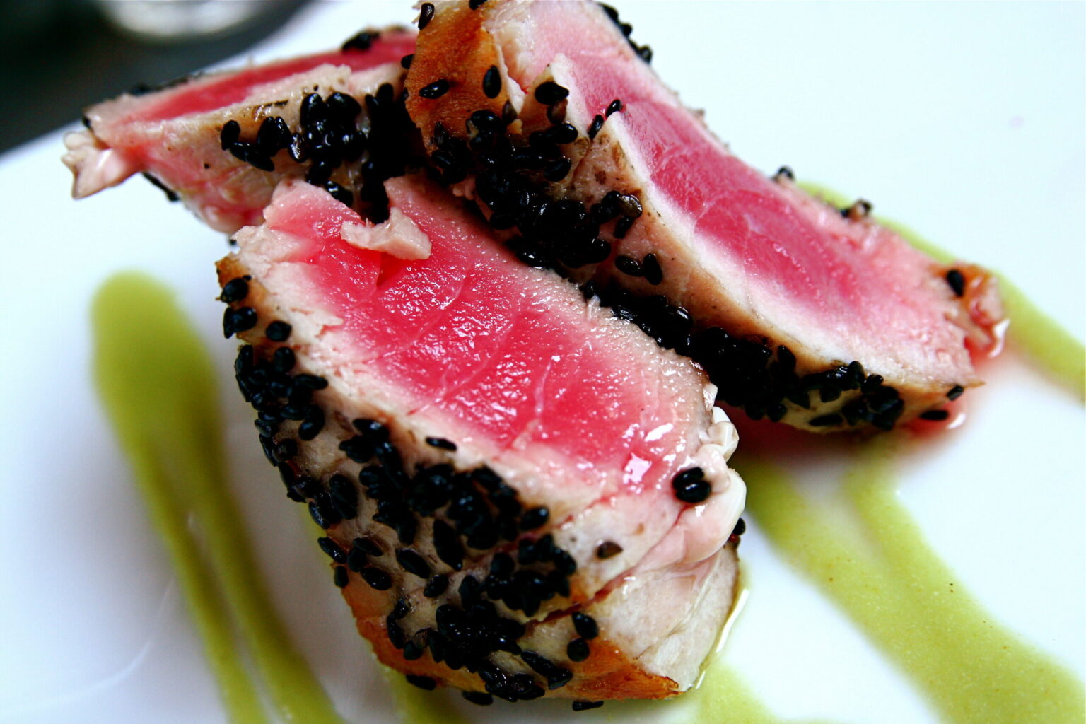 Close-up of seared tuna slices with a black sesame crust, a thin cooked band and a rare pink center