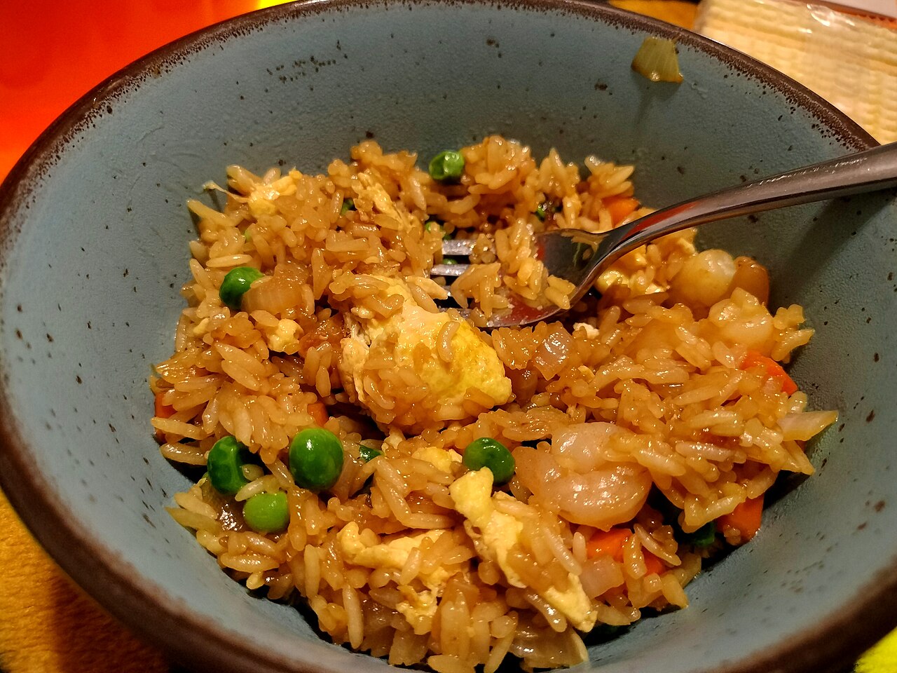 Homemade shrimp fried rice in a bowl with scrambled egg, green peas and pink shrimp