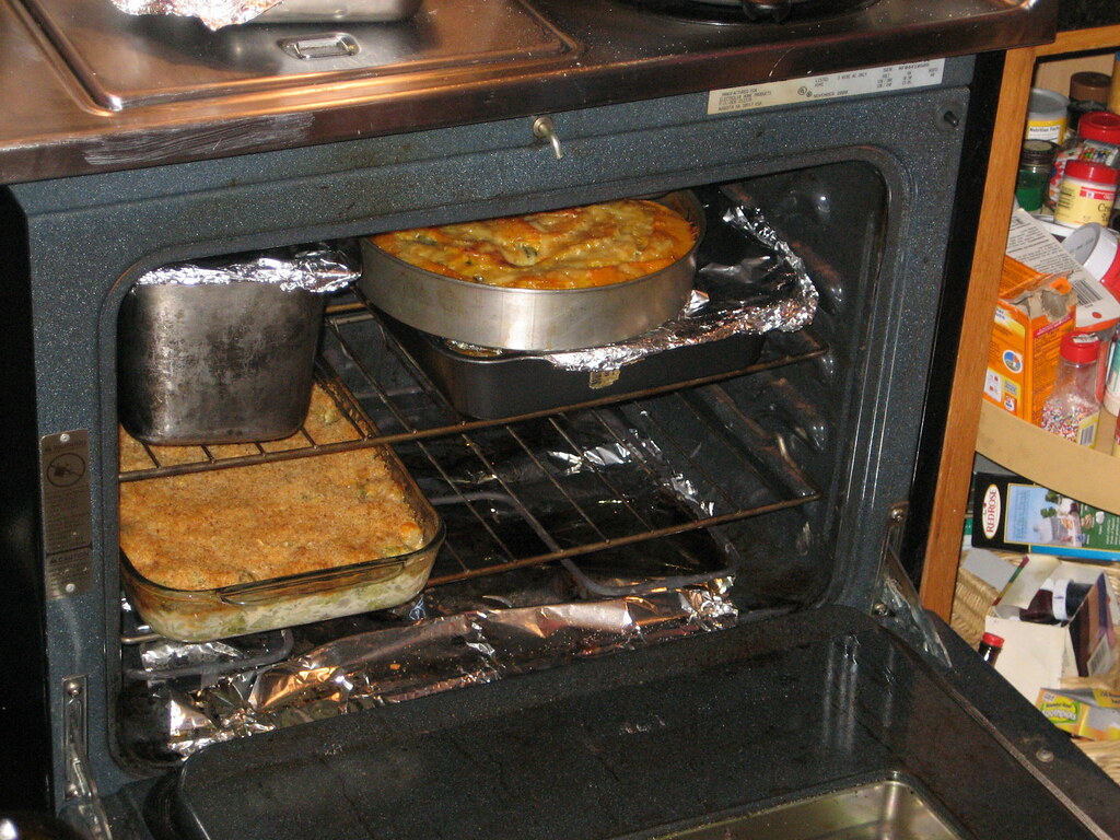 An open oven with several Thanksgiving side dish casseroles baking on two racks